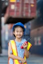 Asian little girl holding walkie- talkie at Container cargo site. Business heir concept.