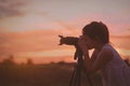 Asian little girl photographer taking picture silhouette sunset sky by digital camera on tripod standing with happy Royalty Free Stock Photo