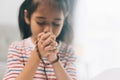 Asian little girl praying with rosary in hand at home Royalty Free Stock Photo