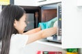 Asian little girl pulls food out of the microwave carefully,cute child with protective gloves on her hands in the kitchen at home