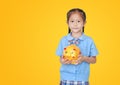 Asian little girl in school uniform holding piggy bank isolated on yellow background with copy space. Schoolgirl with money saving Royalty Free Stock Photo