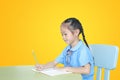 Asian little girl in school uniform writing on notebook at desk isolated over yellow background. Schoolgirl and Education concept Royalty Free Stock Photo