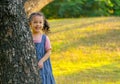 Asian little girl stay behind the big tree and smile with morning light in garden Royalty Free Stock Photo