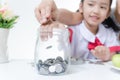 Asian little girl in Thai student uniform putting coin to glass