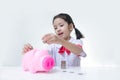 Asian little girl in Thai student uniform putting coins to piggy Royalty Free Stock Photo