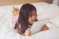 Asian little girl using tablet computer in bed.