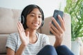Asian little girl video call with a headset on the smartphone and waving in greeting while sitting in the living room at home.