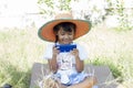 Asian girl wearing father`s straw hat sitting happy with the using of mobile phone to play games in the garden while waitin Royalty Free Stock Photo