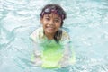 Asian little girl wearing swimming goggles and holding a kickboard is practicing to float happily in the pool. Royalty Free Stock Photo