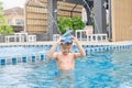 Asian little kid in swimming goggles and snorkel learning to swim at outdoor pool in summer day Royalty Free Stock Photo