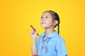 Asian little schoolgirl in school uniform holding Red dipped paintbrush thinking of drawing something over yellow background Royalty Free Stock Photo