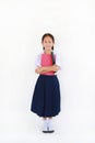 Asian little young girl child in Thai school uniform standing with hugging a book and big pencil isolated on white background. Royalty Free Stock Photo