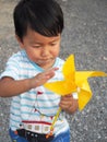Asian lovely kid turning yellow windmill toy by hand with small stones background.