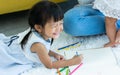 Asian lovely little daughter girl playing with fun and happiness in living room at indoor home, smiling, using color pencils to Royalty Free Stock Photo