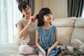 Asian loving mother spend leisure time with young little girl daughter in living room in house. Caring mom combing small child`s h