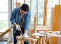 Asian male carpenter woodworker engineer in jeans outfit with safety gloves and glasses goggles using hand saw cutting wood stick Royalty Free Stock Photo