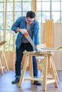 Asian male carpenter woodworker engineer in jeans outfit with safety gloves and glasses goggles using hand saw cutting wood stick Royalty Free Stock Photo