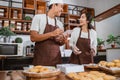 Asian male chef holding order book while chatting with female chef while preparing donut orders