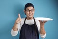 Asian Male Chef or Waiter Shows Empty White Plate, Presenting Something, Copy Space Royalty Free Stock Photo