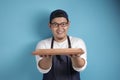Asian Male Chef or Waiter Shows Empty Wooden Plate, Presenting Something, Copy Space Royalty Free Stock Photo