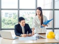 Asian male chief architect or engineer in suit and young female discuss on blueprint on desk Royalty Free Stock Photo