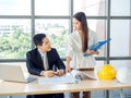 Asian male chief architect or engineer in suit and young female discuss on blueprint on desk Royalty Free Stock Photo