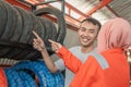Asian male consumer looks at a tire by pointing a finger selecting a tire with a veiled female mechanic