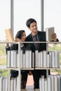 Asian male and cuacasian female university students standing at bookshelf seaching and reading book in library