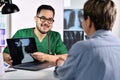 Asian male doctor in surgical uniform consulting and explaining female patient using laptop in examination room Royalty Free Stock Photo