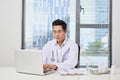 Asian male doctor typing on laptop computer while sitting at the Royalty Free Stock Photo