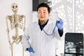 Asian male doctor in white coat, protective gloves and stethoscope in his hand, standing in his office with big human Royalty Free Stock Photo
