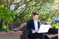Asian male entrepreneur freelancer sitting outdoors in city park a bench talking online a video call using laptop Business man Royalty Free Stock Photo
