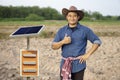 Asian male farmer stands beside mini solar panel.