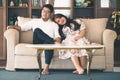 Asian male and female couples, in which men wear white shirts and women wear floral dresses, smiling while sitting on a sofa in a Royalty Free Stock Photo