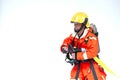 An Asian male firefighter in red protective uniform, mask and helmet with fire extinguisher standing on white backgrond.