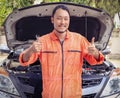 Asian Male mechanic wearing orange color jumpsuit working on car engine outdoor, standing in front of car holding wrench and