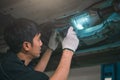 Asian male mechanical hold and shining flashlight to examine car under chassis of automotive vehicle. Safety suspension inspection