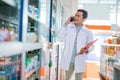 Asian male pharmacist in uniform taking call and holding clipboard Royalty Free Stock Photo