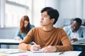 Asian male student sitting at desk in classroom writing exam Royalty Free Stock Photo