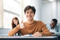 Asian male student sitting at desk showing thumbs up gesture Royalty Free Stock Photo