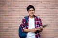 Asian male students wear plaid shirts. Standing next to a brick wall, carrying a backpack, carrying books, school supplies,