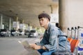 Asian male tourist reading map while waiting for taxi on bus stop with suitcases Royalty Free Stock Photo