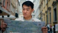 Asian male tourist traveling in new city standing outdoors looking at paper map in search of location using travel guide Royalty Free Stock Photo