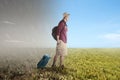 Asian man with a backpack and suitcase standing on the meadow field with a different climate