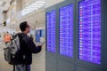 Asian man with backpack traveler using the smart mobile phone for check-in at the flight information screen in modern an airport Royalty Free Stock Photo