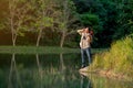 Asian man with bagpack and binoculars or other accessories for travel action of shout or bawl and stand near lake during camping