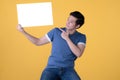 Asian man in casual clothes holding empty blank board and pointing finger isolated on yellow background Royalty Free Stock Photo