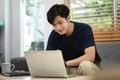 Asian man in casual clothes sitting on couch in bright living room and using laptop computer Royalty Free Stock Photo