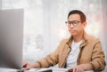 Asian man in casual clothing using a laptop communicates on the internet with the customer at  kitchen table at home. concept work Royalty Free Stock Photo