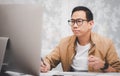 Asian man in casual clothing using a laptop communicates on the internet with the customer at  kitchen table at home. concept work Royalty Free Stock Photo